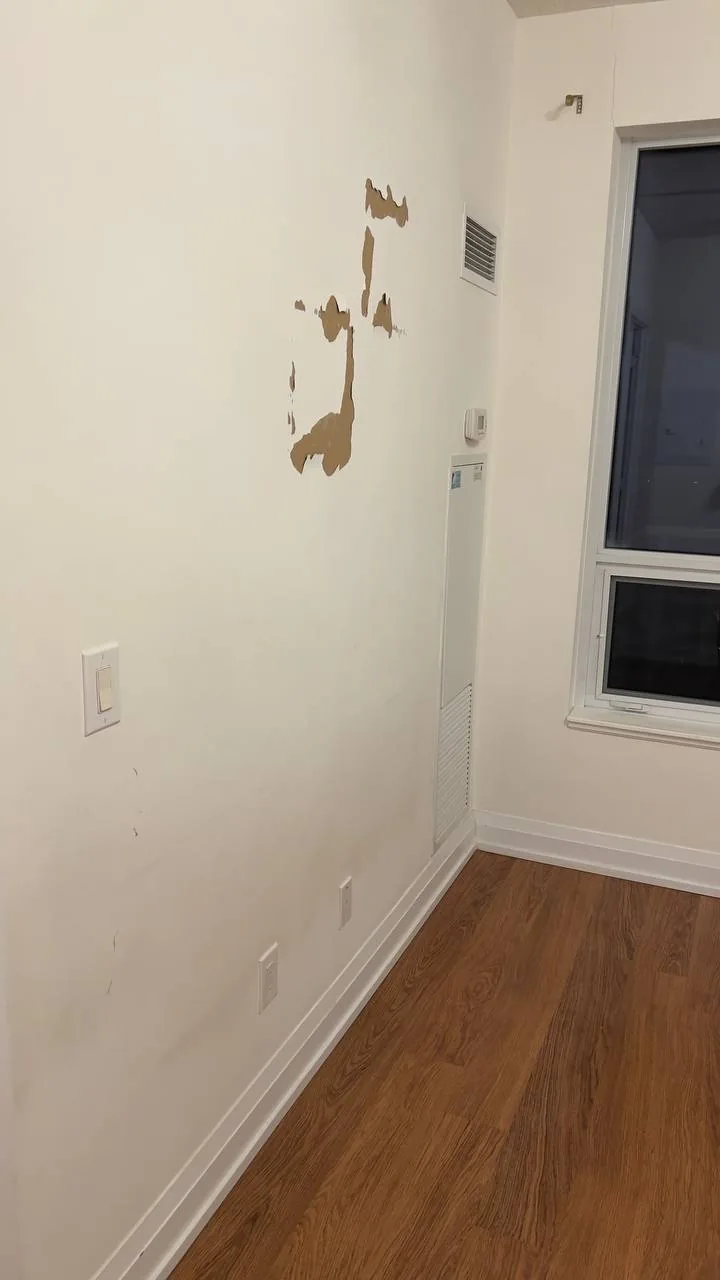 Damaged drywall wall with torn patches before repair