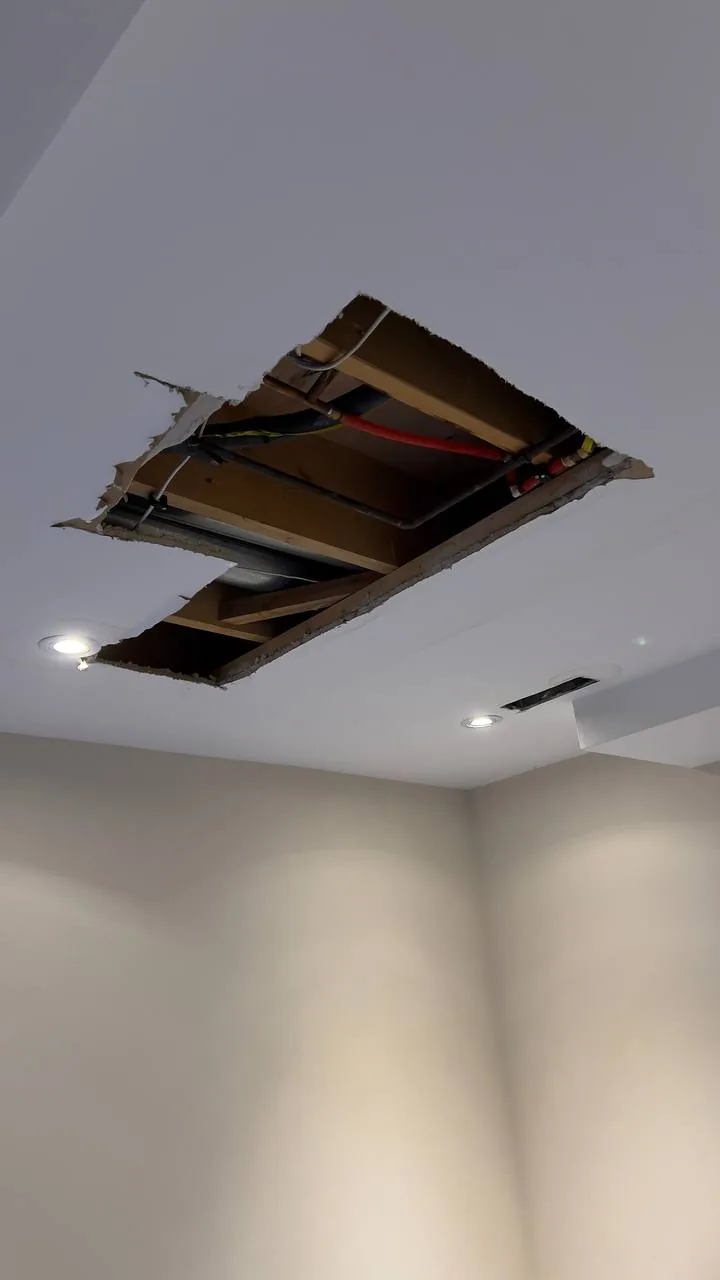 Ceiling with a large hole exposing framing and pipes before repair